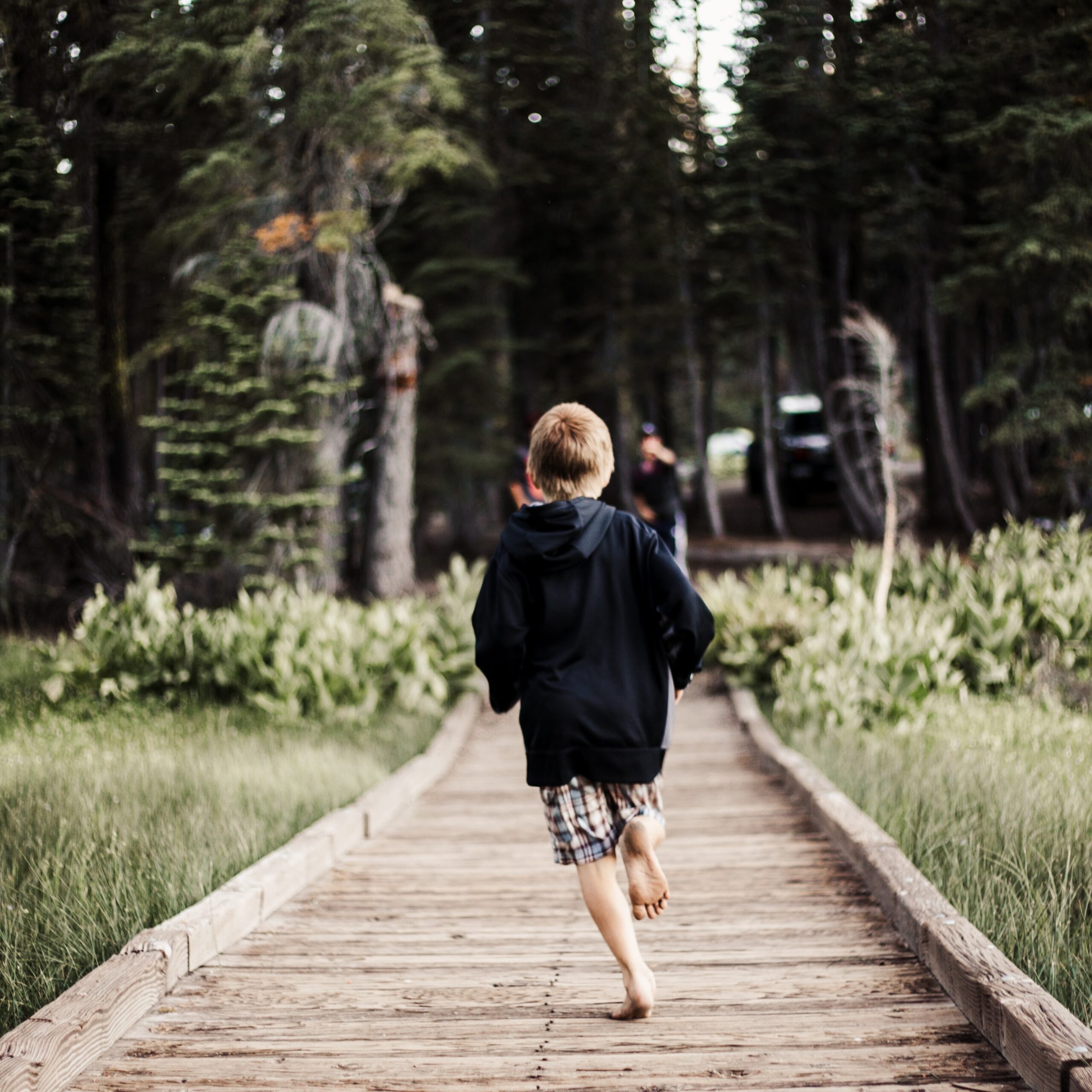 boy running on a bridge towards the woods